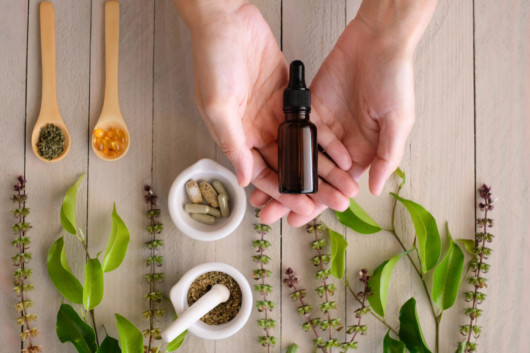 A bottle of cbd oil lies in the hands with herbs and leaves on the wooden background