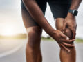 Closeup shot of a sporty man who is holding his injured knee pain while exercising outdoors