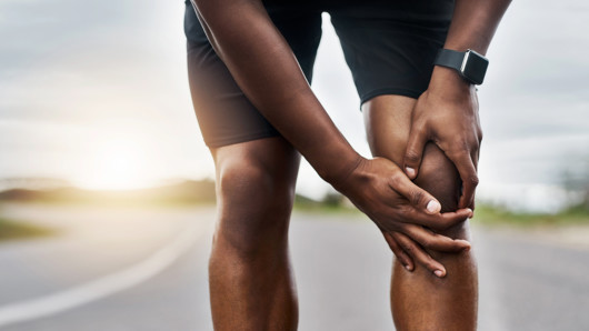 Closeup shot of a sporty man who is holding his injured knee pain while exercising outdoors