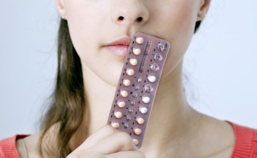 A young girls holds birth control pills close to her face