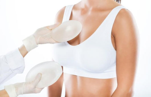 The doctor is holding two breast implants and showing to the girl who wants to do breast augmentation.