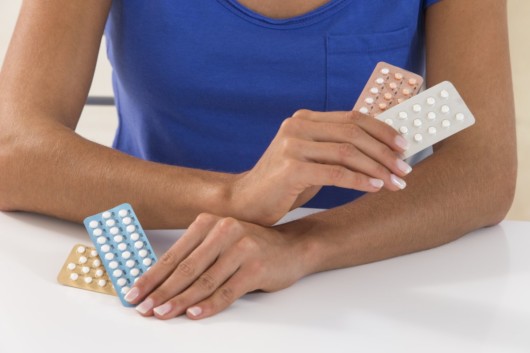 Girl holding different birth control pills and thinking which to choose