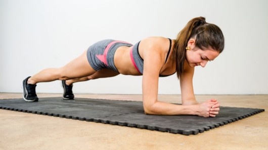 A fir girl is doing plank in the room as an isometric exercise 