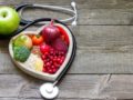 Fruits, vegetables and grains are in the white plate on wooden background next to stethoscope
