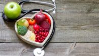 Fruits, vegetables and grains are in the white plate on wooden background next to stethoscope