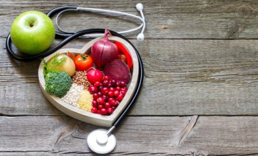 Fruits, vegetables and grains are in the white plate on wooden background next to stethoscope