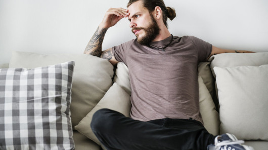 A guy sitting on the sofa with his fingers on his forehead and thinking deeply