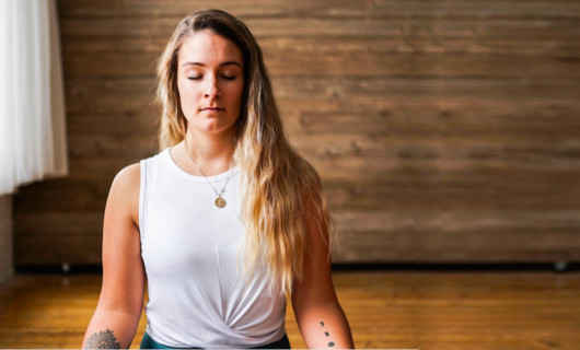 A young girl is sitting and meditating in the room with her eyes closed