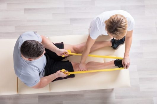 A guy is working out with a resistance band and physiotherapist 