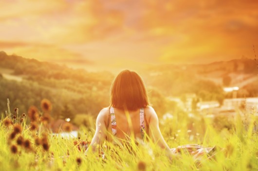 A relaxed girl is sitting with her back to the cam on the ground and overview the nature