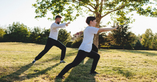 a man and a woman in white t-shirts and black pants are doing tai chi outdoor