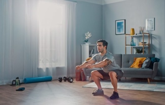 A guy is exercising in his home gym. A guy is doing squats in the room