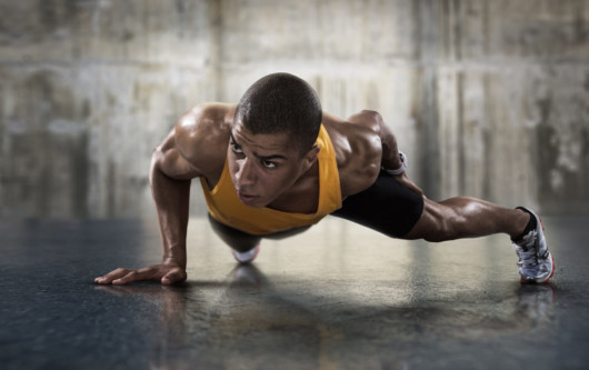 a fit and strong guy in yellow undershirt is doing bodyweight workout on the floor