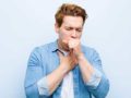 Man in blue t-shirt on blue background has deep coughing