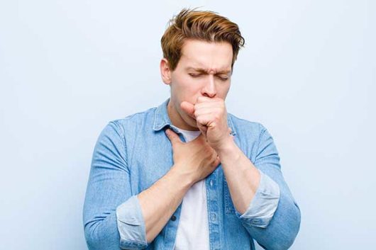 Man in blue t-shirt on blue background has deep coughing