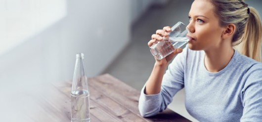 A girl in blue sweater is sitting at the wooden table and drinking water