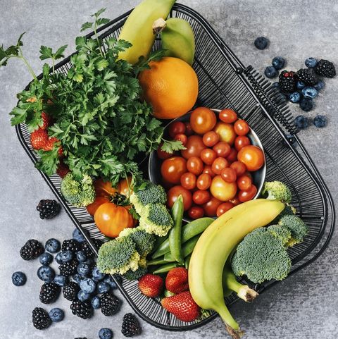 A black basket with greens, fruits and vegetables on the grey table