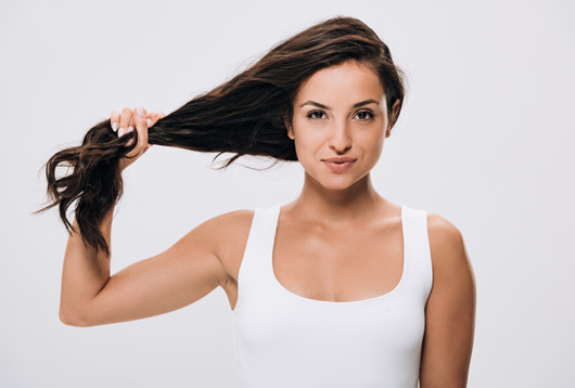 A beautiful girl in white undershirt is holding her brown strong and healthy hair in her hand