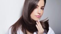 Beautiful girl on grey background is holding her healthy hair in hands