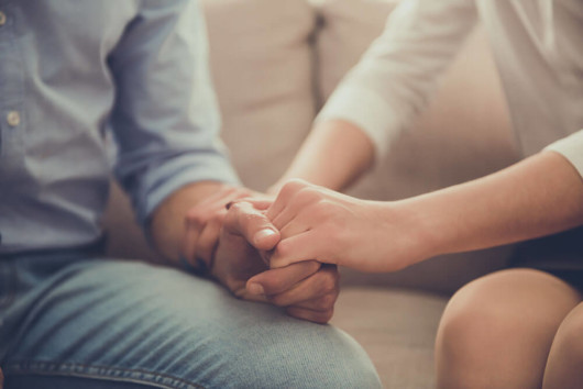 A man and a woman are holding hands in hands and sitting on the sofa