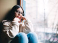 A sad girl sits on the window sill and looking into the window