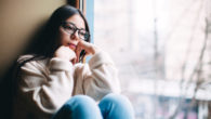 A sad girl sits on the window sill and looking into the window