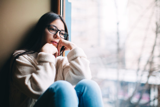 A sad girl sits on the window sill and looking into the window