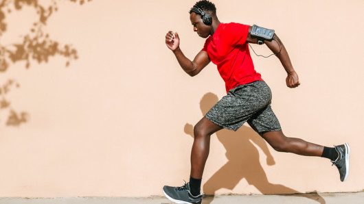 A black guy in red t-shirt and headphones is running on the street