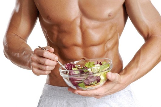 A strong and muscly guy holding a plate with vegetables