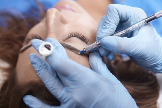 microblading close-up, hands adding pigment to eyebrows.