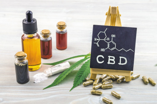 Full spectrum Cannabidiol CBD oils, capsules and crystals isolate with small blackboard with CBD word and chemical structure on wooden backdrop