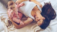 Young mom is lying on the bed smiling and playing with a kid