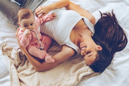 Young mom is lying on the bed smiling and playing with a kid