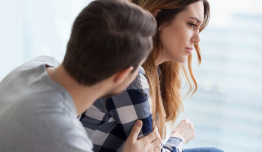 A man is trying to calm down a woman. The man is sitting next to the sad woman on the white background