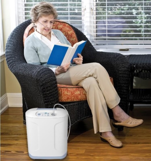 An old lady is reading in the black chair with an oxygen generator