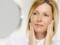 A beautiful woman on white background is looking into the mirror after the facelift procedure