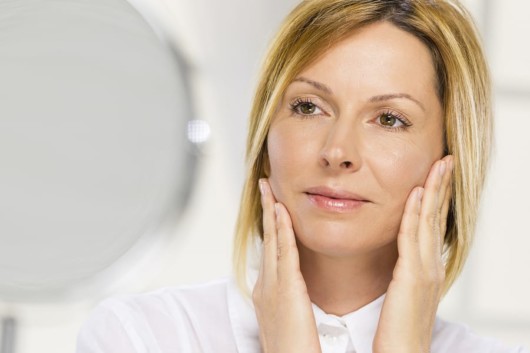 A beautiful woman on white background is looking into the mirror after the facelift procedure