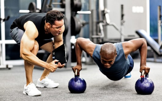 personal trainer is cheering up the man who is doing push ups on the kettlebells 