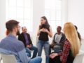 A young girl stands and talking in front of the people in the rehab