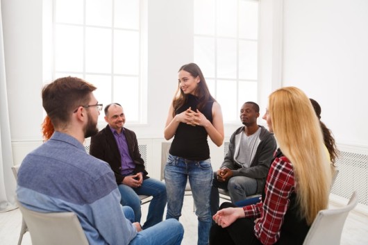 A young girl stands and talking in front of the people in the rehab