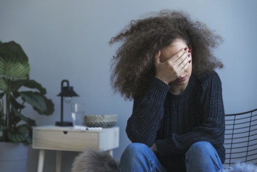 A girl is sitting and covering her eyes with a hand. The girl is sad and depressed