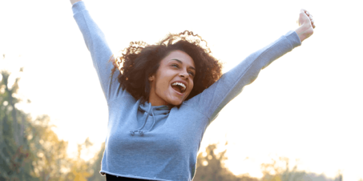 A happy girl in blue sweater is smiling and stretching her hands into the air