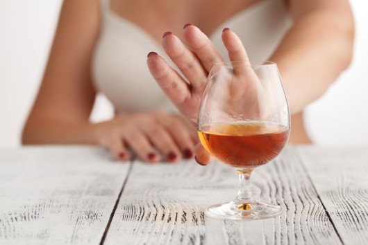The girl shows she doesn't want to drink alcohol putting her hand in front of the glass with alcohol