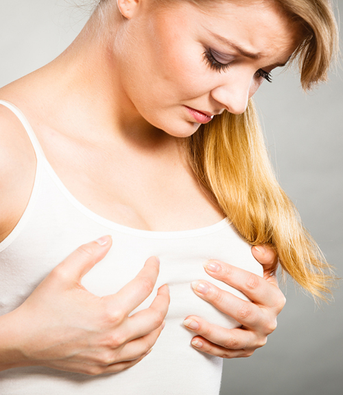 Beautiful girl in white undershirt on white background is holding her breasts in her hands in paid. Girl has pain in her breasts 