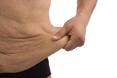 A man on the white background is holding his loose skin throughout the midsection. 