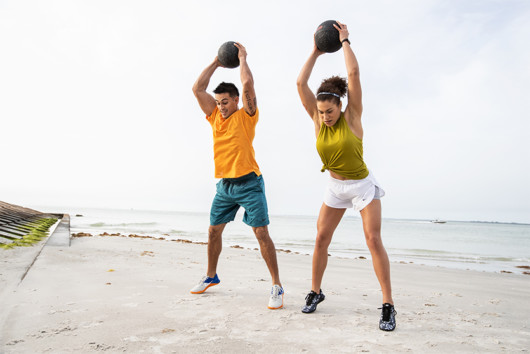 A sporty couple performing HIIT workout with medicine balls on the beach