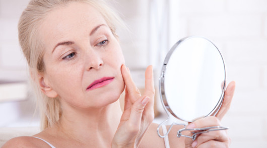 A lady is looking in the mirror and touching her face