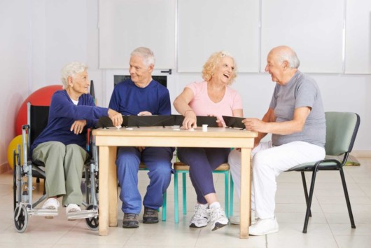 Four senior people are sitting at the table talking and playing a table game