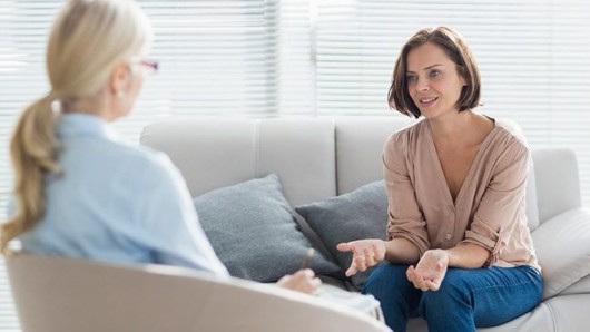 A young woman is sitting on the sofa and talking to a counselor 