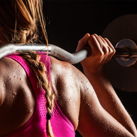 Girl in pink sports bra with barbell on her shoulders ready to workout